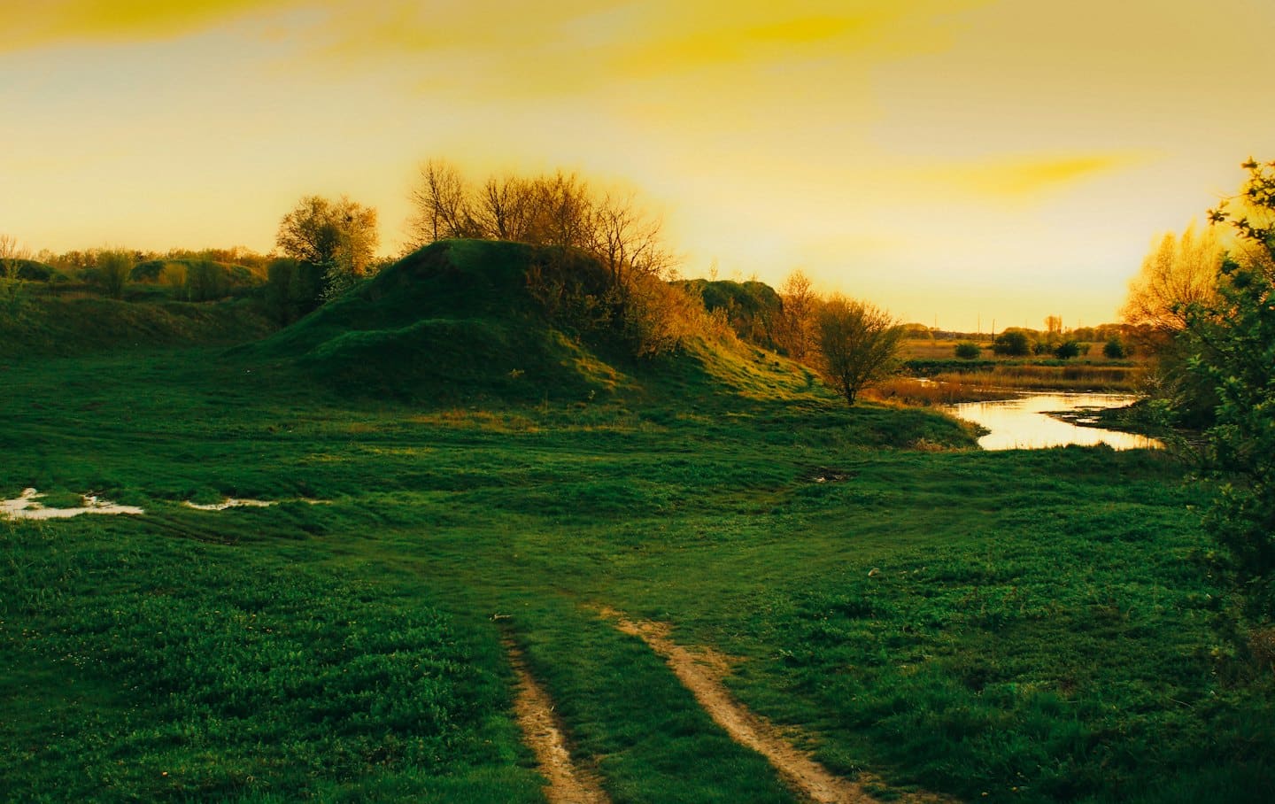 A dirt path winds through rolling hills toward a lake.
