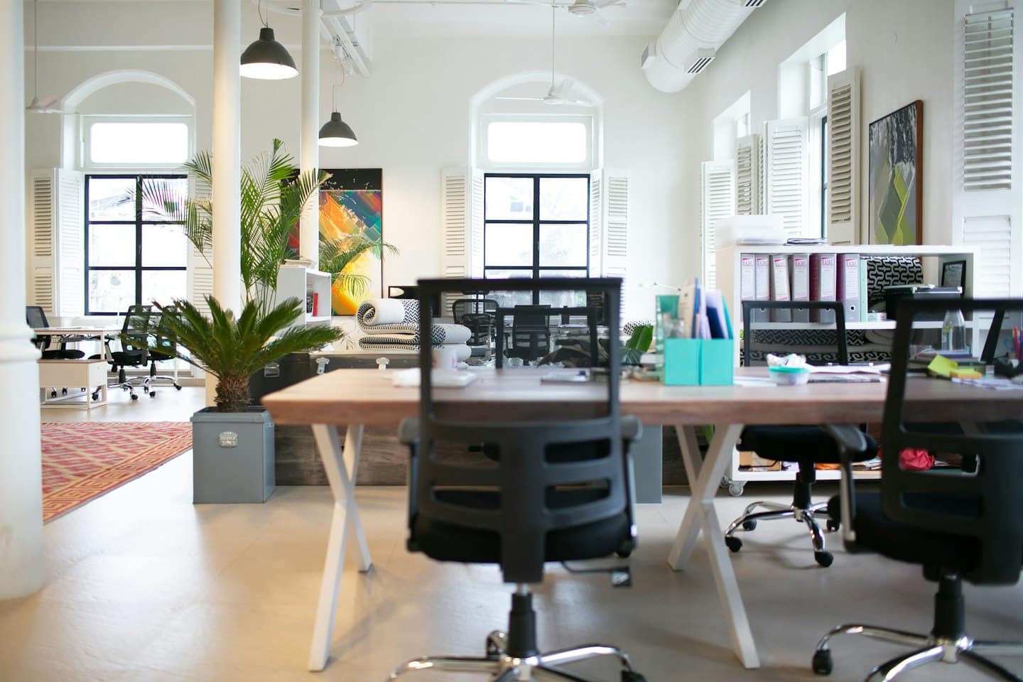 Modern open-plan office with light wood desks and large windows.